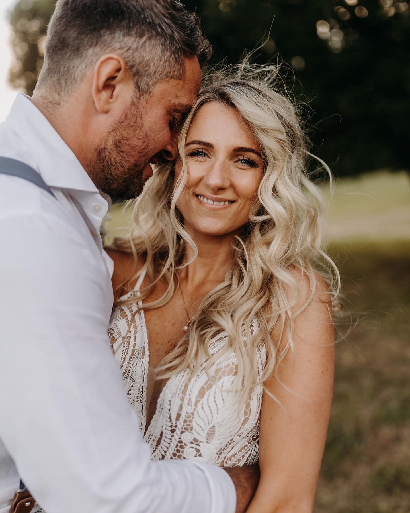 Une mariée blonde aux cheveux détachés et bouclés dans le vent. Elle a un maquillage très solaire.