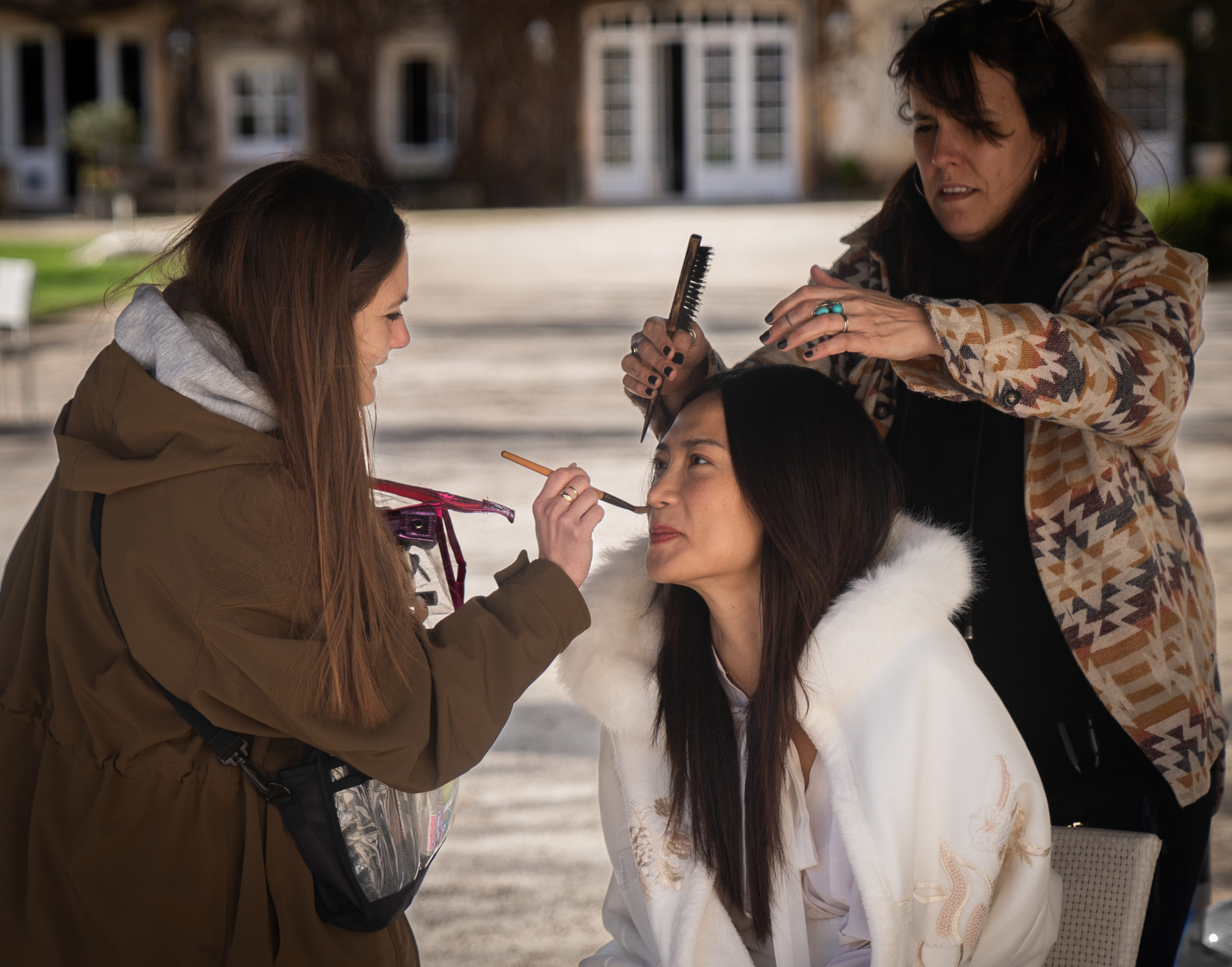 Julia Marty fait une retouche maquilage à une comédienne. Il y a également une coiffeuse qui raccorde la coiffure de la comédienne.