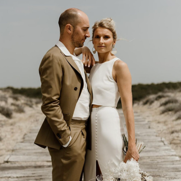 Un couple de mariée sur plage. La mariée est blonde et la peau dorée. Elle porte un maquillage très naturel effet no-makeup.