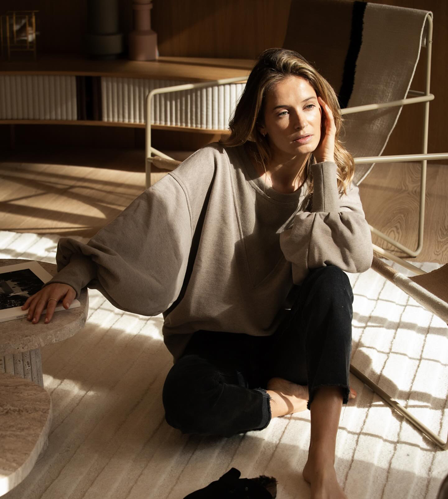 Une jeune femme blonde aux cheveux détachée, assise sur le sol et regarde vers l'extérieur. Elle a un maquillage et naturel.